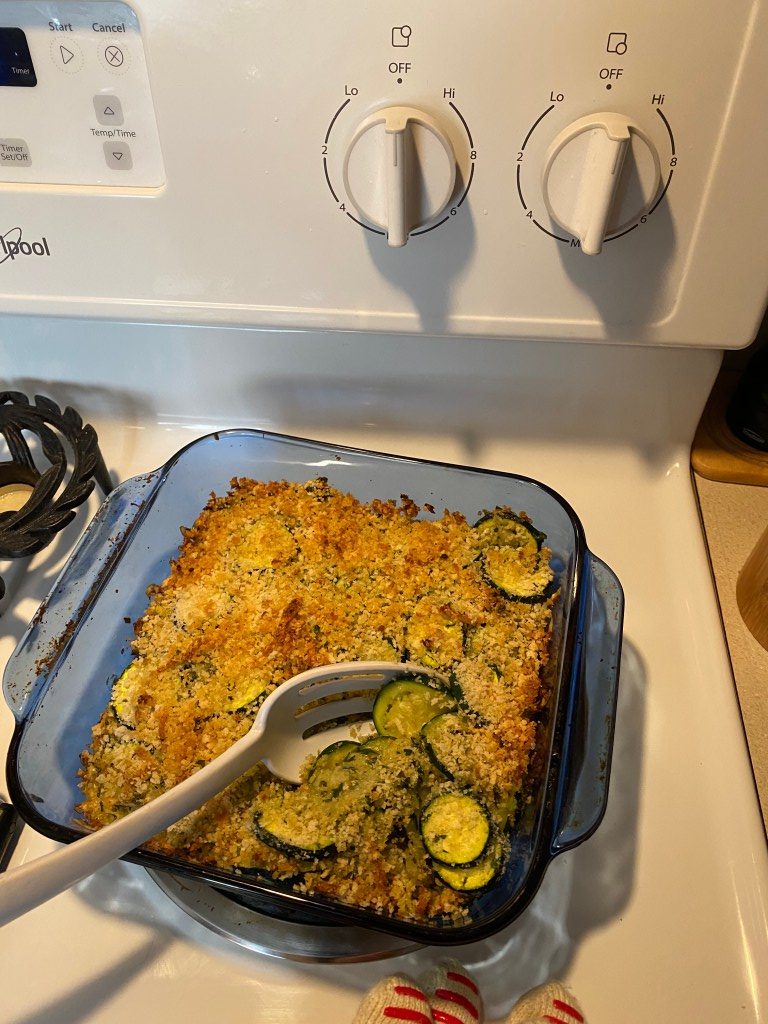 summer squash gratin in a blue baking dish with a spoon breaking through the crumb crust showing the squash layers