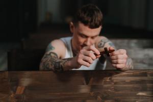 A white tattooed man kneeling holding a small wooden cross.